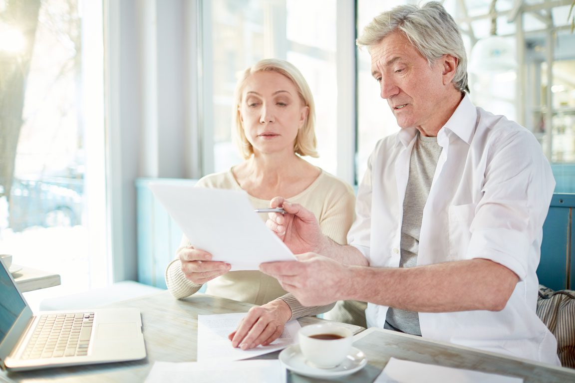 senior couple filling out forms in front of laptop